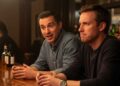 Two guys are talking at a bar, with one looking offended by what the other has said.