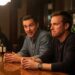 Two guys are talking at a bar, with one looking offended by what the other has said.